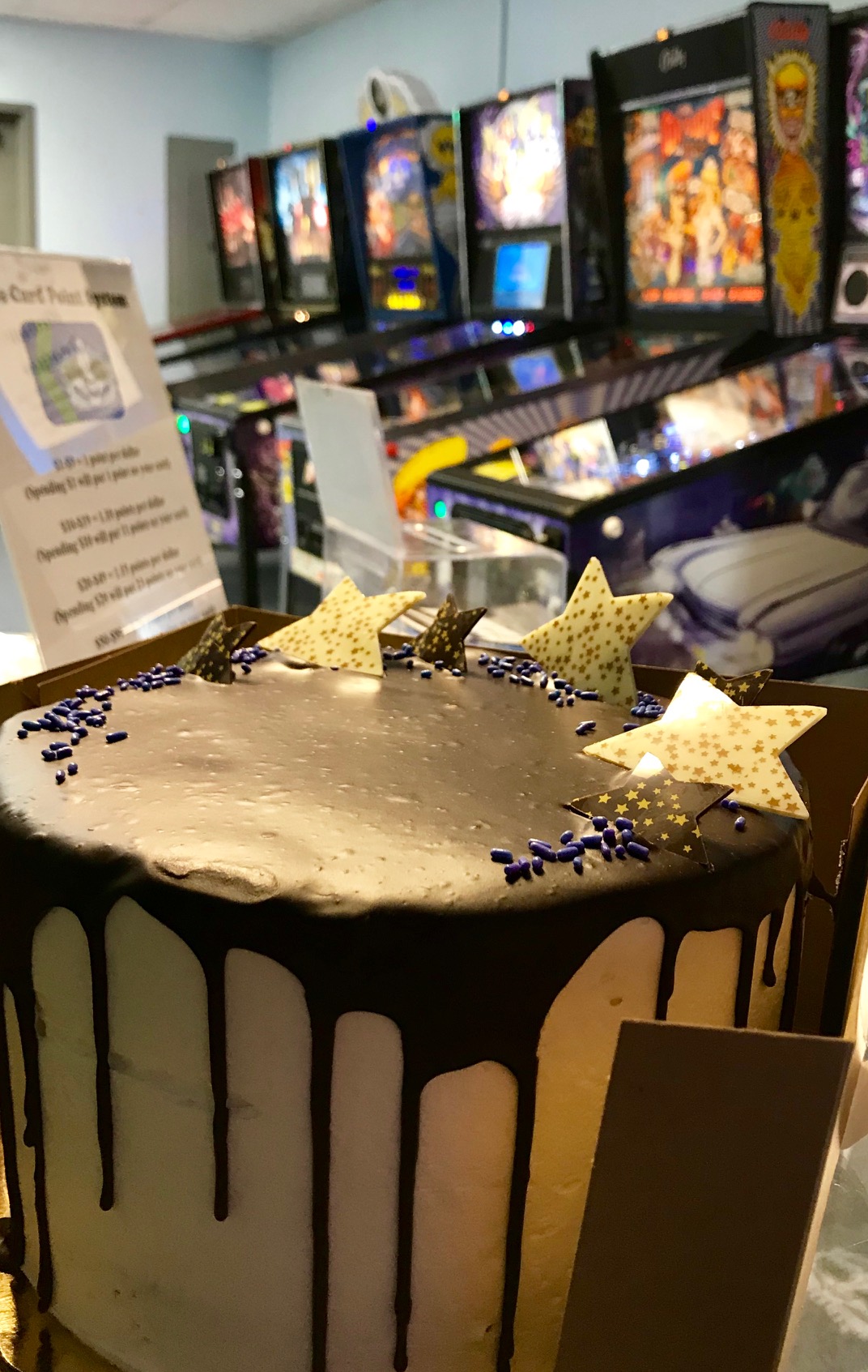 Party cake centered in frame before pinball machines in background.