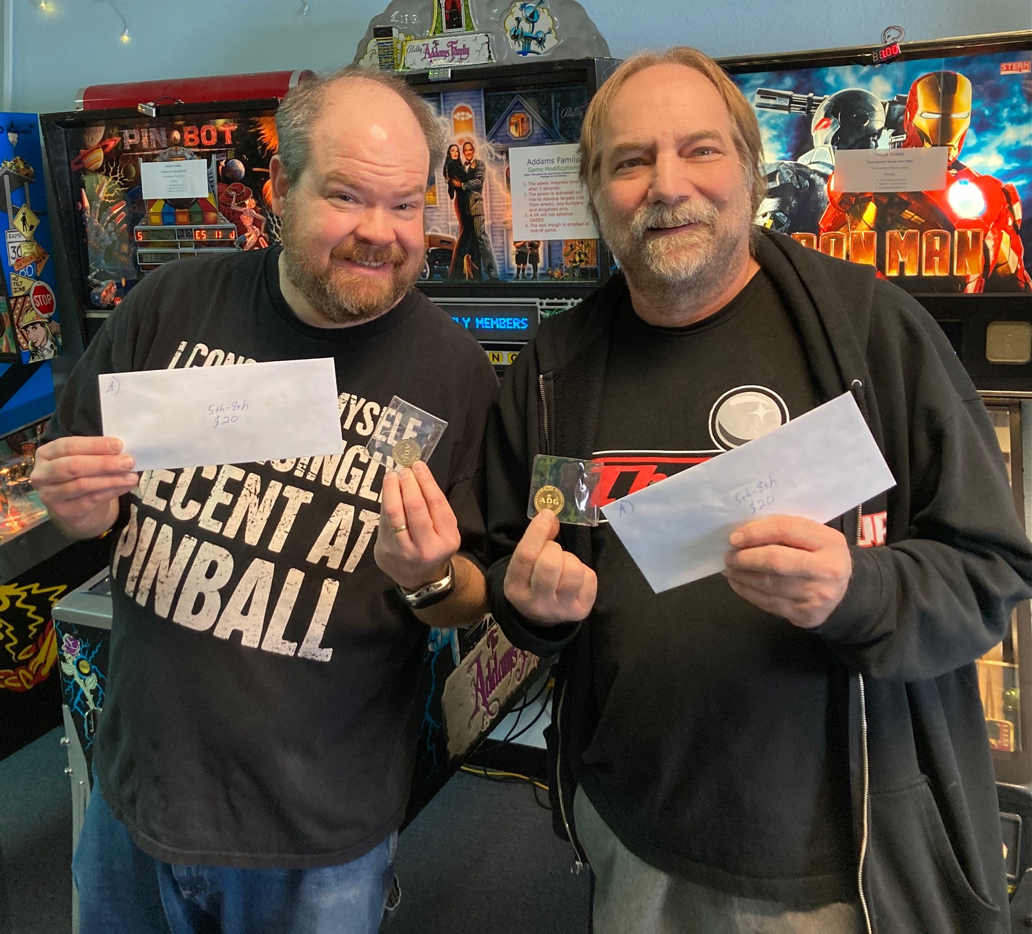 Two men holding envelopes in front of pinball machines.