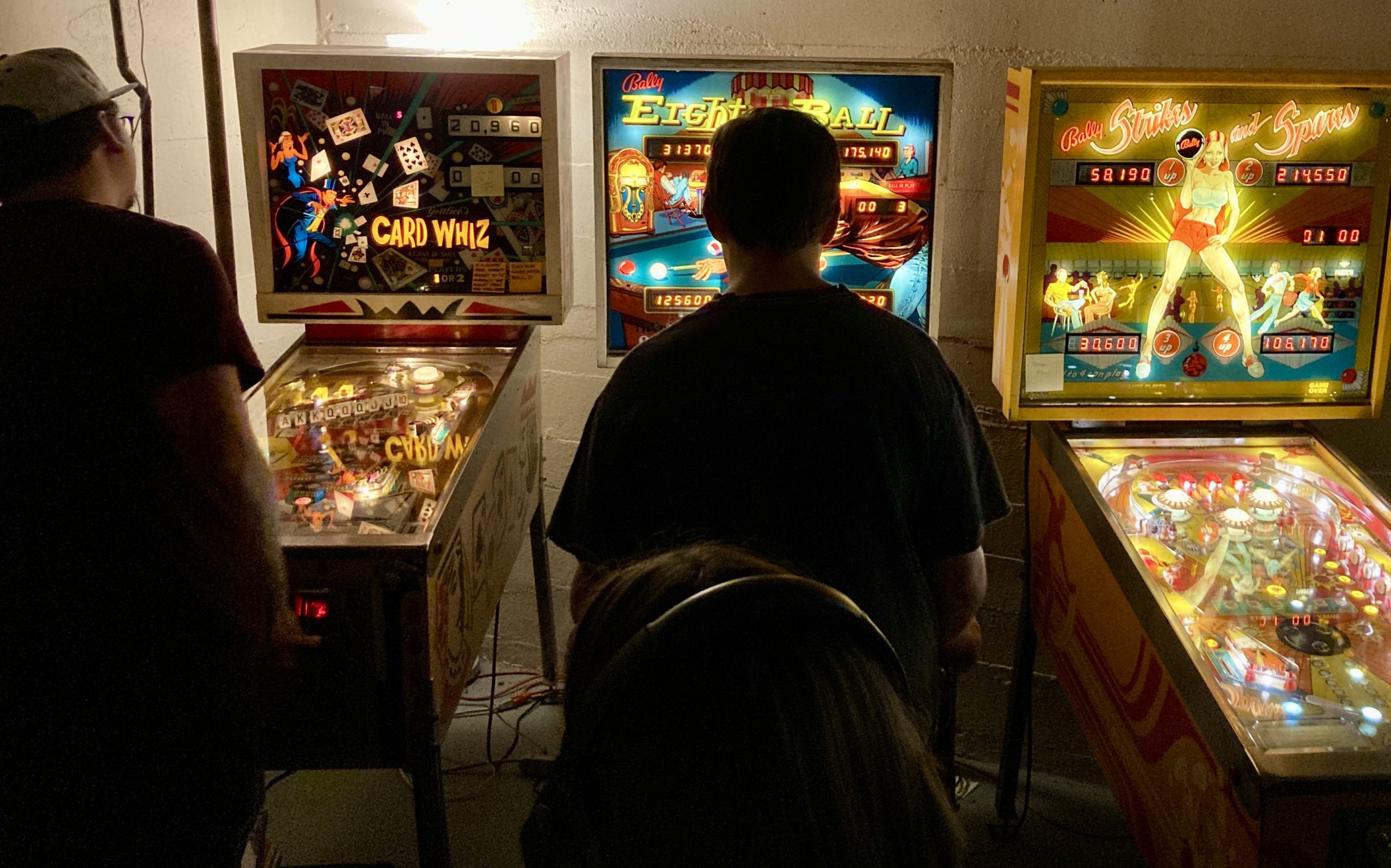 A picture of a person playing pinball from behind at a tournament at Lyons Classic Pinball in honor of Dean Grover.