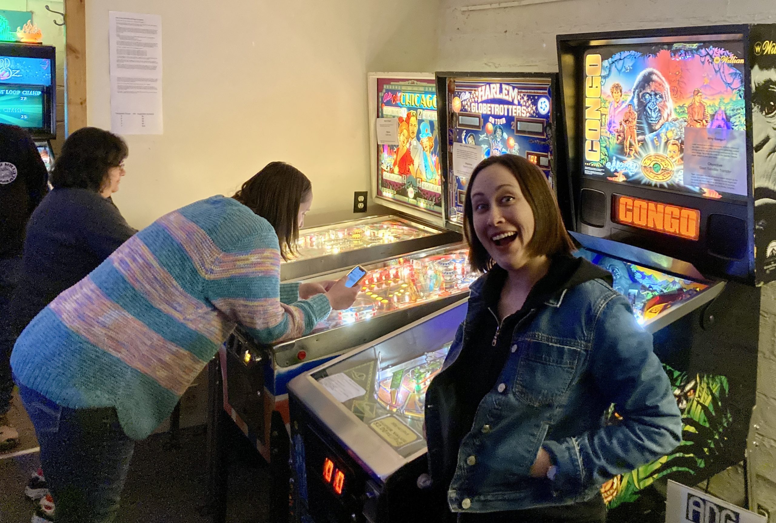 People playing pinball, woman is in foreground smiling.