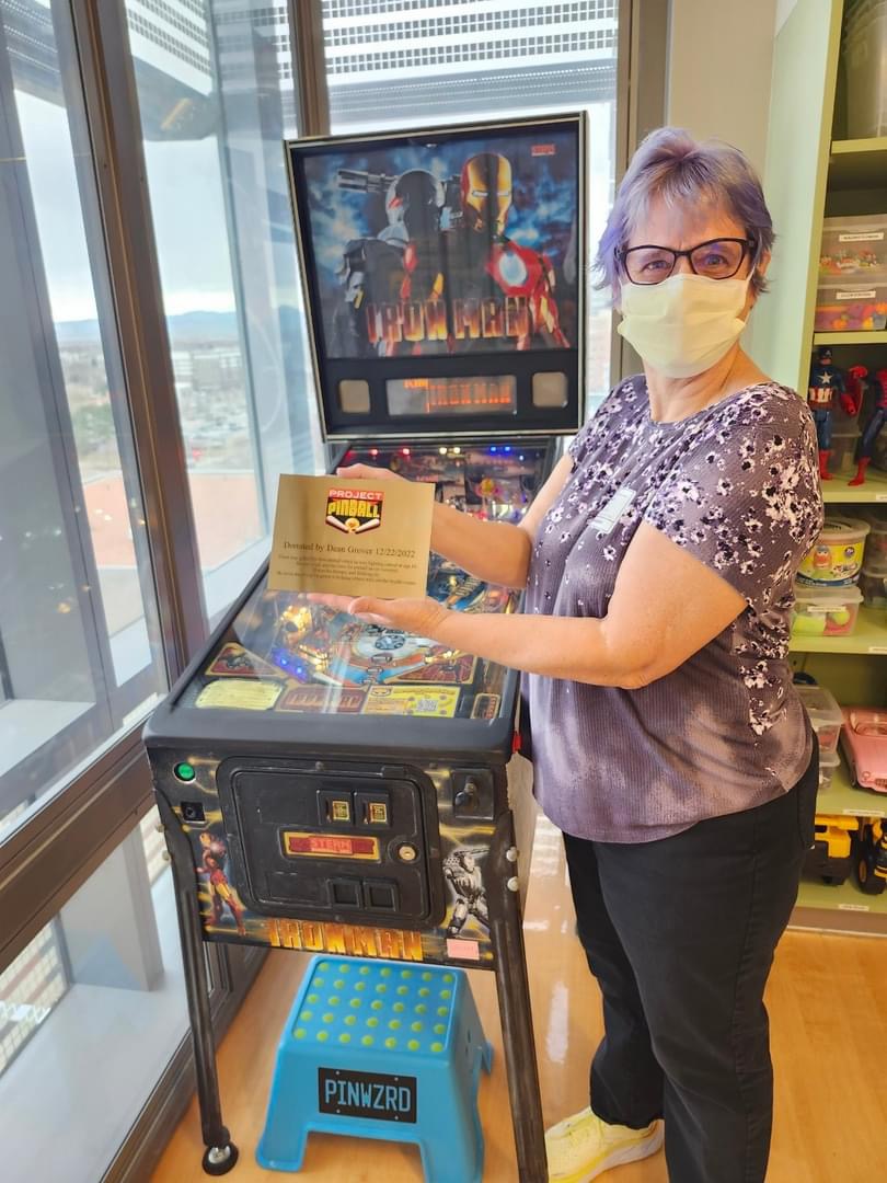Dean's wife Sam hold Dean's Plaque in front of the Iron Man pinball machine.